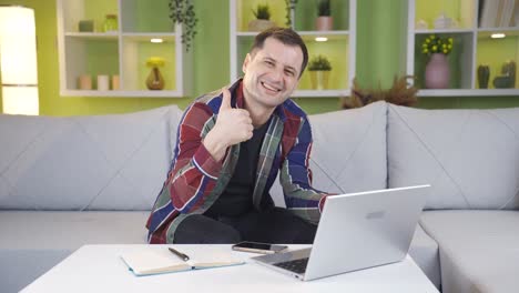Man-making-positive-gesture-with-hand-while-smiling-at-camera-while-working-on-laptop.